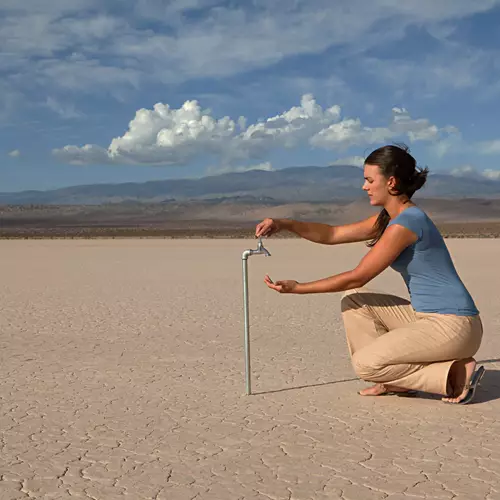 Woman looking for water at a tap in a desert area