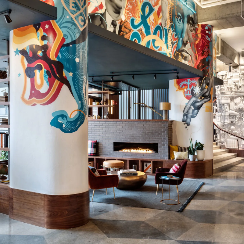 A lobby with a fireplace, seating area, and colorful murals on the walls.